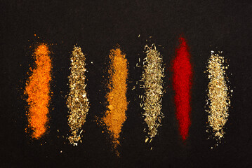 Spices scattered on a black background. Coriander, marjoram, paprika, thyme and rosemary, a universal seasoning, heaped on a dark background.