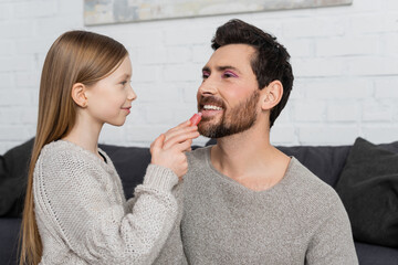 happy preteen girl applying shiny lip gloss on lips of smiling and bearded father.
