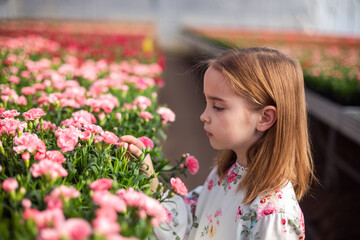 Happy cute adorable blondie caucasian little girl with flowers in greenhose. Eco friendly gardening