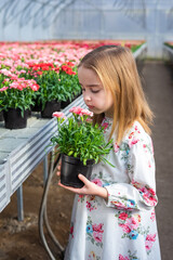 Happy cute adorable blondie caucasian little girl with flowers in greenhose. Eco friendly gardening