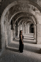 a girl in black clothes walks through antique arches