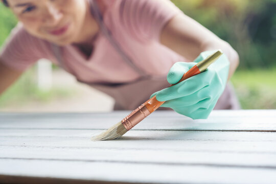 Female hand with a brush to apply white paint on wooden furniture. The concept of renovation, the furniture update. Carpentry, wood treatment, hard at work, home improvement, do-it-yourself concept.
