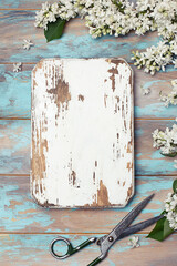 Old wooden board, vintage scissors and white lilac flowers on blue rustic wooden background. Spring flowers composition with copy space