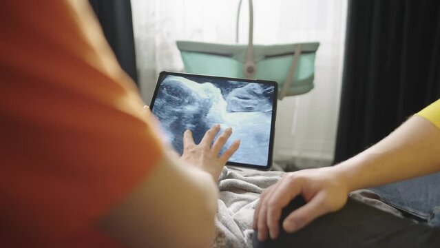 Pregnant couple looking at photo of baby in belly at home on sofa. A man and a woman who are expecting a child are happy together. High quality 4k footage