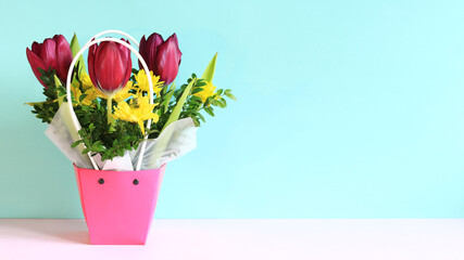 Bouquet of spring flowers with tulips in a pink basket. Spring flowers on a blue background. Flowers with empty space nearby. Photo to create postcards