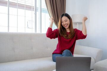 Happy young Asian business woman successful excited raised hand rejoicing with laptop at home.