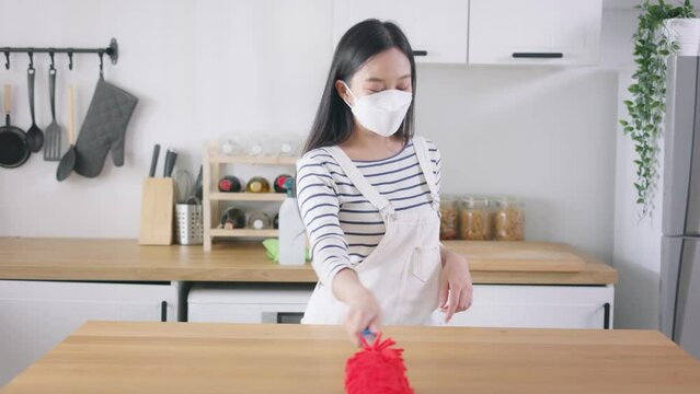 Young happy Asian woman cleaning home, wearing a mask and having fun. Beautiful cleaning service worker housekeeping and tidying up the kitchen. Housework and chores concept