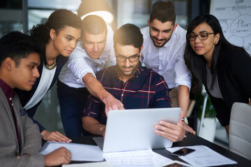 They work seamlessly together. Shot of a group of colleagues working together around a laptop in an office.