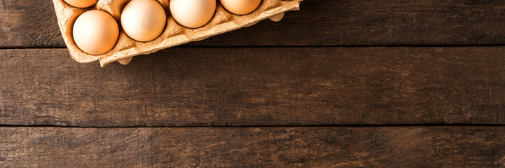 Fresh eggs in carton box on wooden background. Top view
