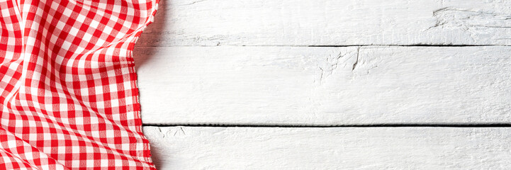 Red checkered tablecloth on white wooden table. Top view