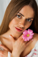 Obraz na płótnie Canvas Portrait of young beautiful long-haired brown-eyed woman with pink gerbera on white background. Spring. Holidays. Mothers Day.