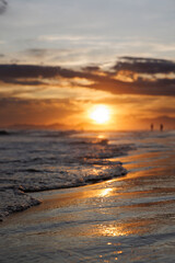 Fototapeta na wymiar lindo por do Sol em segundo plano com as ondas do Mar cobrindo a areia da praia em primeiro plano 