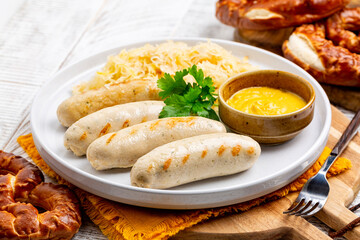 Bavarian white sausage Weisswurst made from minced veal and pork back bacon, crauti or sauerkraut, mustard and a soft pretzel. German food.  Light wooden table.