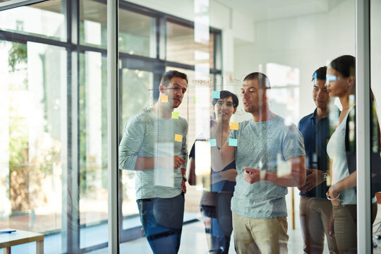 Planning is the first step. Cropped shot of a group of young designers planning on a glass board.