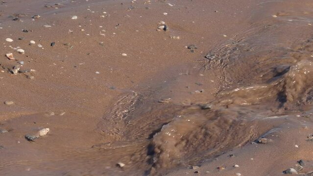 wave drops on the beach, detail of sea water running over brown sand