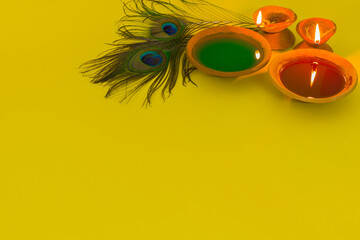 happy holi celebration with colors, clay lamp and peacock feather symbolizing hindu god krishna....