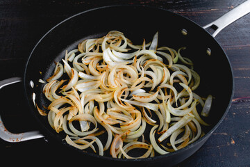 Sliced Onions Browning in a Large Saute Pan: Sweet onion slices browning in olive oil in a skillet