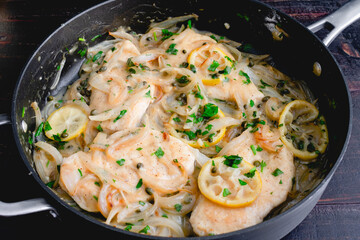 Fototapeta na wymiar Chicken Piccata Cooked in a Large Saute Pan: Chicken cutlets and lemon slices cooked in a white wine sauce with capers