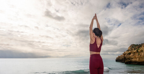 Woman standing by the ocean with her arms raised meditating, head space concept.