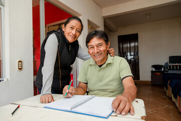 Hispanic adult couple studying together - teacher teaching senior to write - couple budgeting at...