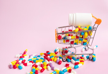 Small shopping cart, trolley with medical pills on pink pastel background. Medicine concept.