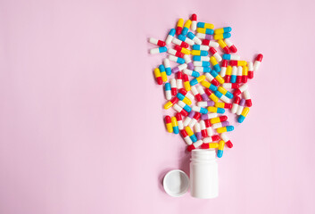 Capsule pills spread out of white plastic drug bottle on pink background. Pharmacy banner. Online pharmacy. Painkiller medicine and antibiotic drug resistance concept.