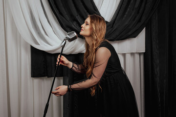 Elegant long haired brunette woman in black dress singing with the static microphone.