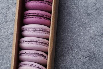Set of violet and lilac macaroons in cardboard gift box on gray concrete background. Top view,...