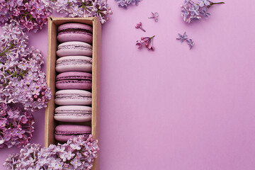 Set of violet and lilac macaroons in cardboard gift box with lilac flowers on violet background....