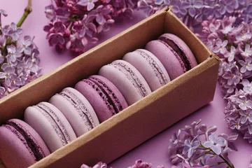 Keuken spatwand met foto Set of violet and lilac macaroons in cardboard gift box with lilac flowers on violet background. Close up view, selective focus. Traditional French dessert © Zygonema