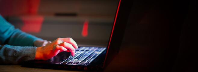 A girl works on a laptop at night, hands on the keyboard.