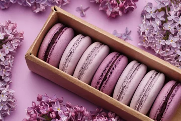 Foto op Aluminium Set of violet and lilac macaroons in cardboard gift box with lilac flowers on violet background. Traditional French dessert © Zygonema