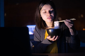 Girl eats noodles and watches video on a laptop.