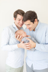 two gay parents dads holding a baby smiling down