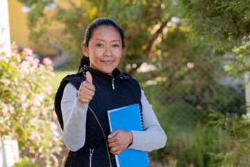 Hispanic woman holding notebooks while raising thumb up proud to learn - Senior adult studying -...