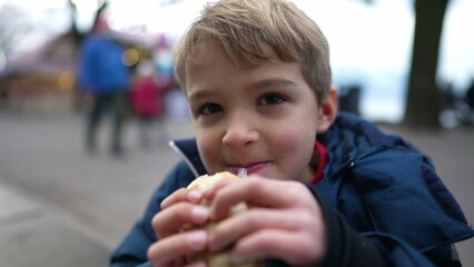 Small boy eating pancake outside in city street during winter season. Hungry child eating food during december festivities