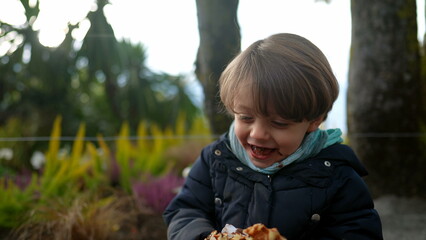 One happy child smiling outside while eating sweet food. Joyful boy during winter season