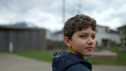 Portrait of a handsome young boy standing outside looking at camera with serious expression. Preteen kid stands outdoors at city park. Tracking shot