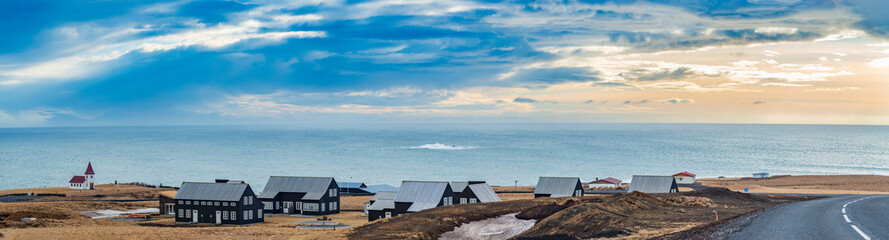 Fototapeta na wymiar Village on the coast of Iceland overlooking the rough sea and picturesque clouds in the background.