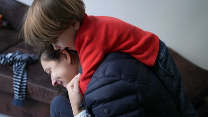 Child embracing mother back. Little boy jumping on parent surprise. Authentic real life love relationship