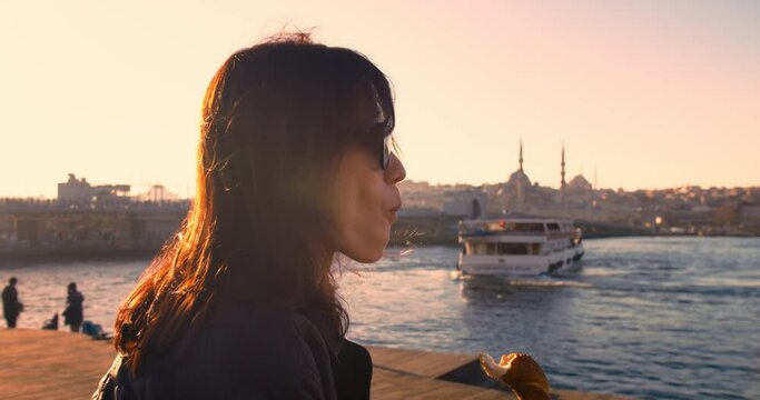 Female traveler eating turkish bagel with istanbul city view at sunrise light, static shot