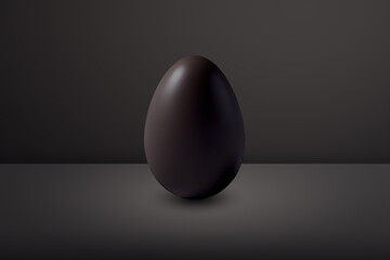 black chocolate Easter egg in front of a black wall and on a black floor