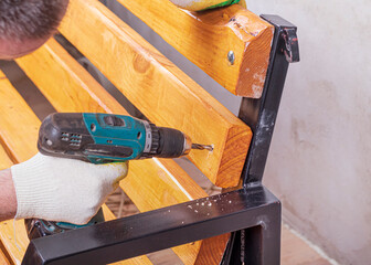 a natural yellow board is lying on a street bench. the master installs the board on a metal frame...