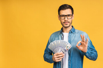 Happy winner! Young rich man in casual holding money dollar bills with surprise isolated over...