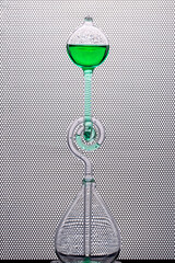 Glass flask with green liquid on the background of round holes