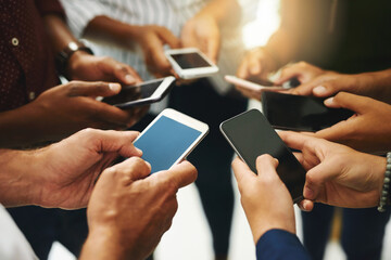 Keeping their successful team connection going. Closeup shot of a group of unrecognizable businesspeople using their cellphones in synchronicity.