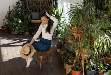 Attractive Asian girl sitting in chair relaxing in garden with many indoor green plants. Green...