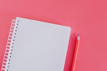 Notebook with a blank page and a pencil on pink background.