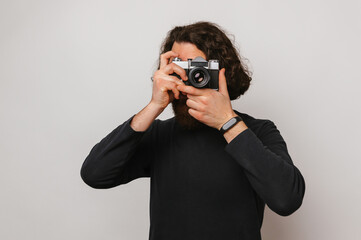 Young bearded man with long brown hair is looking though a vintage camera.