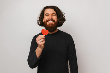 Excited bearded man with long hair is holding a red heart shaped paper.